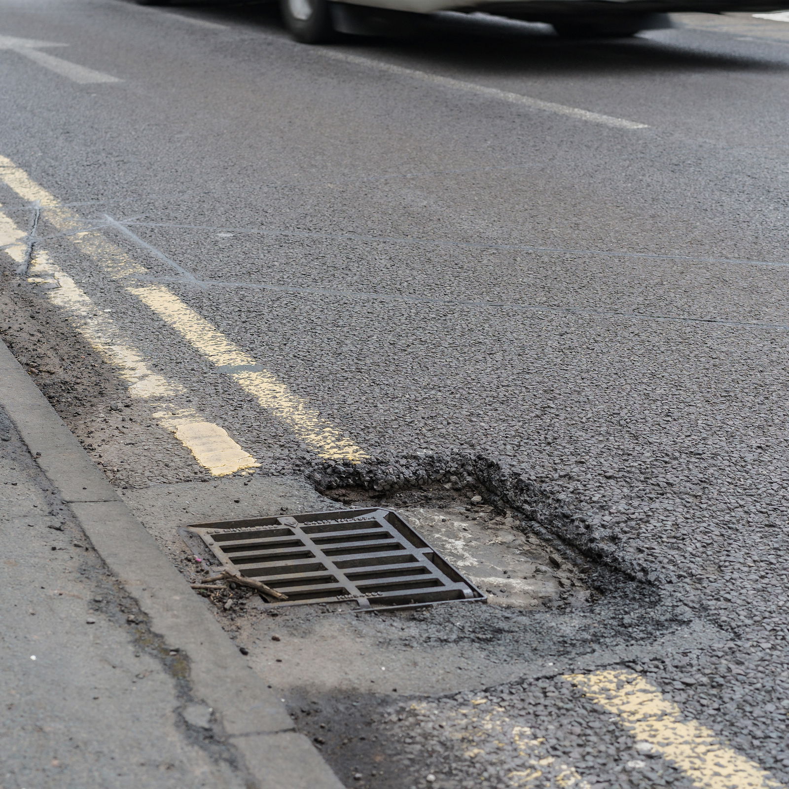 A pothole which has formed around the frame of a gully grating