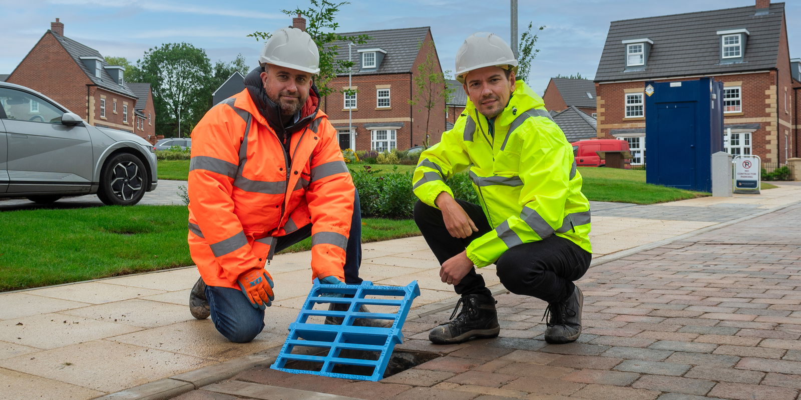 Two men posing next to blue gully grating