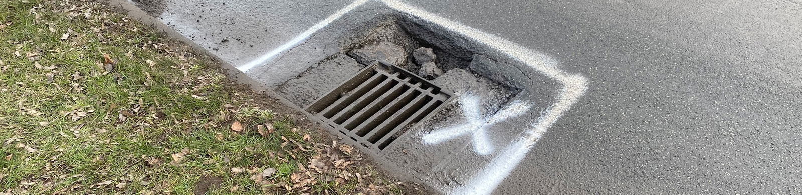 A pothole formed around a gully grating, with spray paint marks
