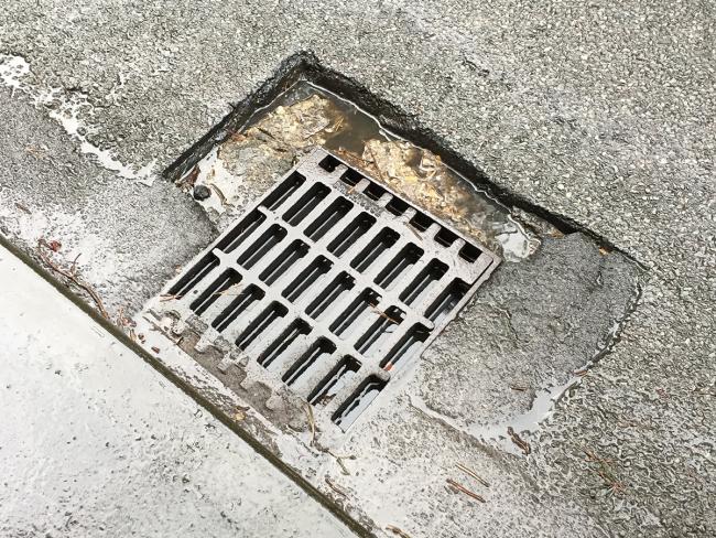 A pothole which has formed around the frame of a gully grating